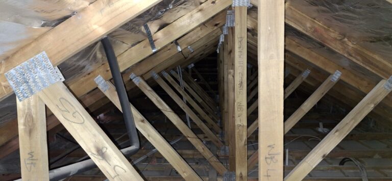 Roof trusses and structural supports in an attic, with visible metal brackets and electrical wiring.